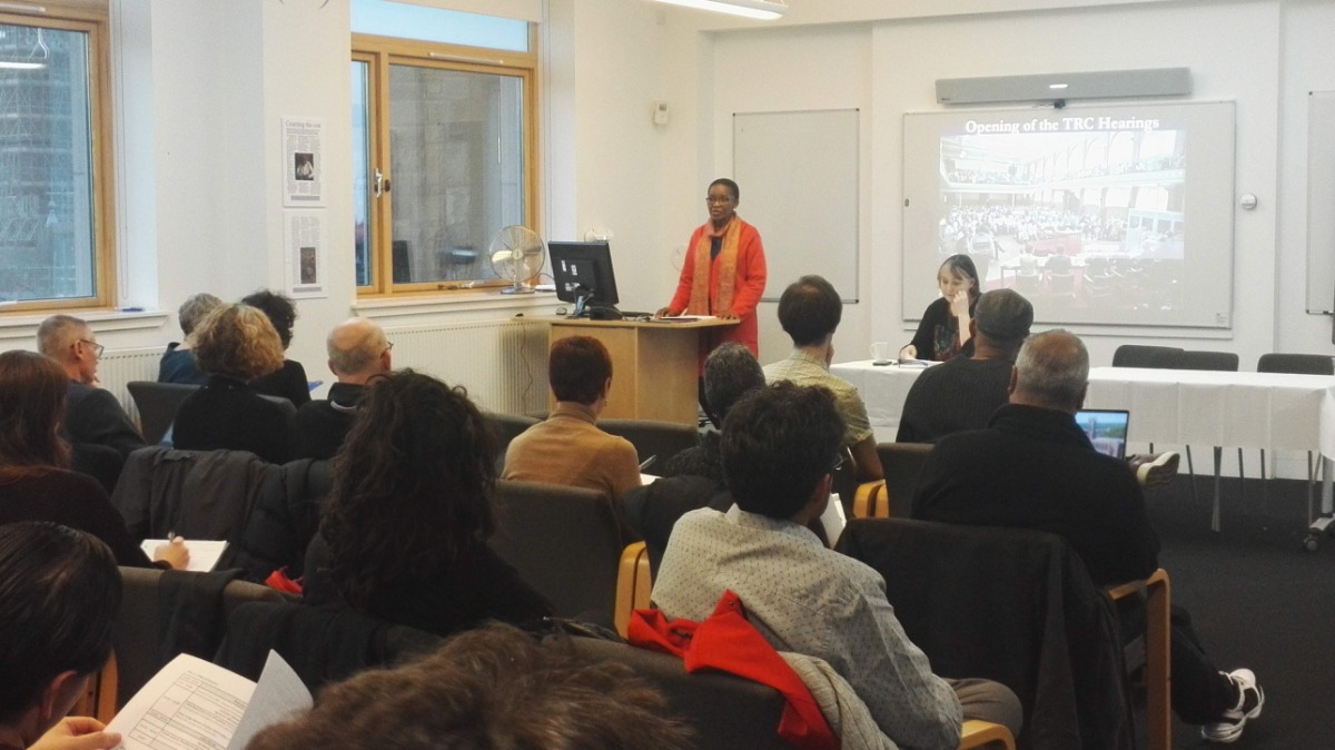 "A person speaking at a conference with a projector screen in the background"