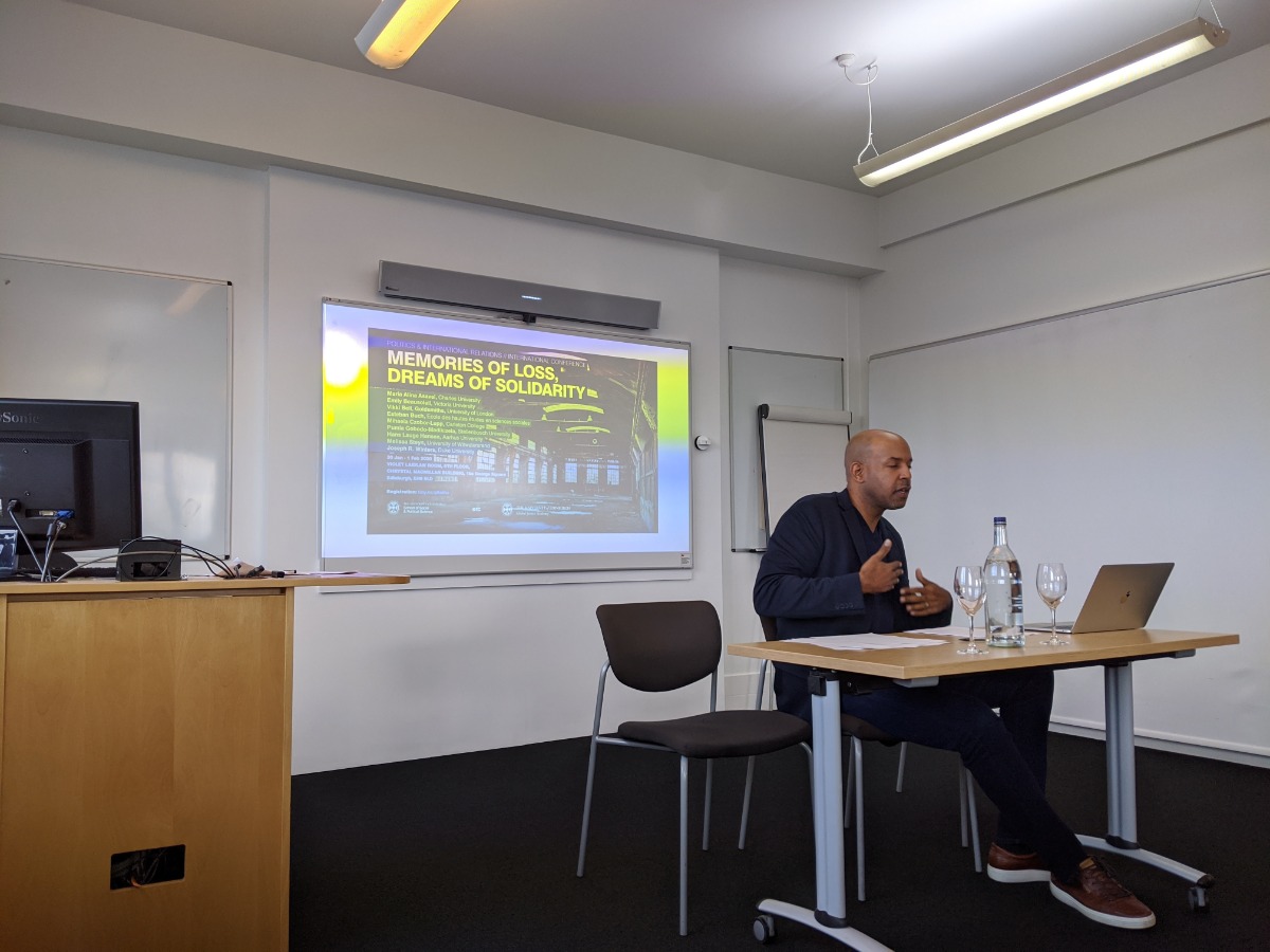 "a man conducting a presentation behind a laptop screen during a conference"